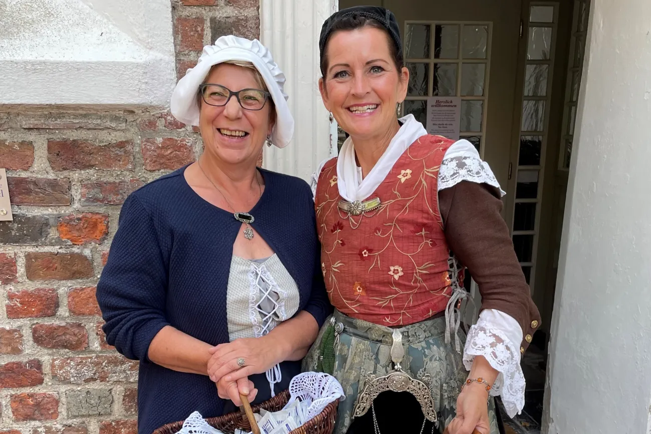Zwei Frauen - Daje und Geeske - in historischen Kostümen lächeln vor einem Backsteingebäude in Greetsiel.
