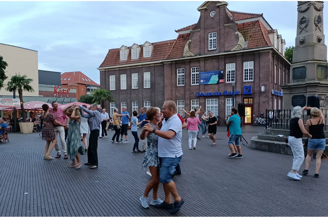 Viele Menschen tanzen paarweise auf dem Denkmalplatz neben einem großen Denkmal.