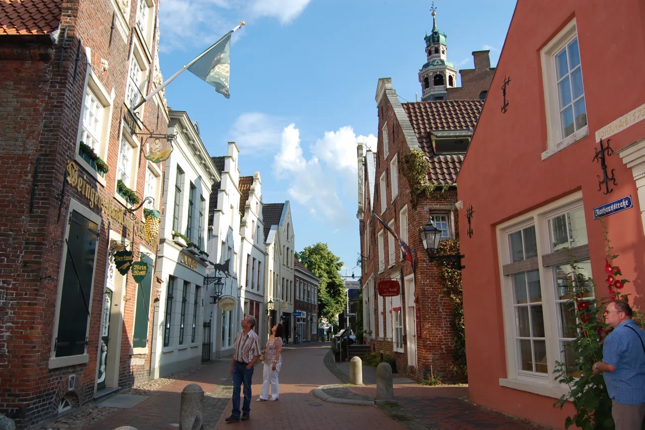 Gepflasterte Gasse in der Altstadt von Leer mit historischen Backsteinhäusern und Passanten bei Sonne.