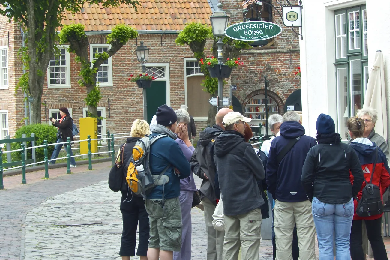 Eine Gruppe Erwachsener steht bei einer Dorfführung auf einer gepflasterten Gasse in Greetsiel.