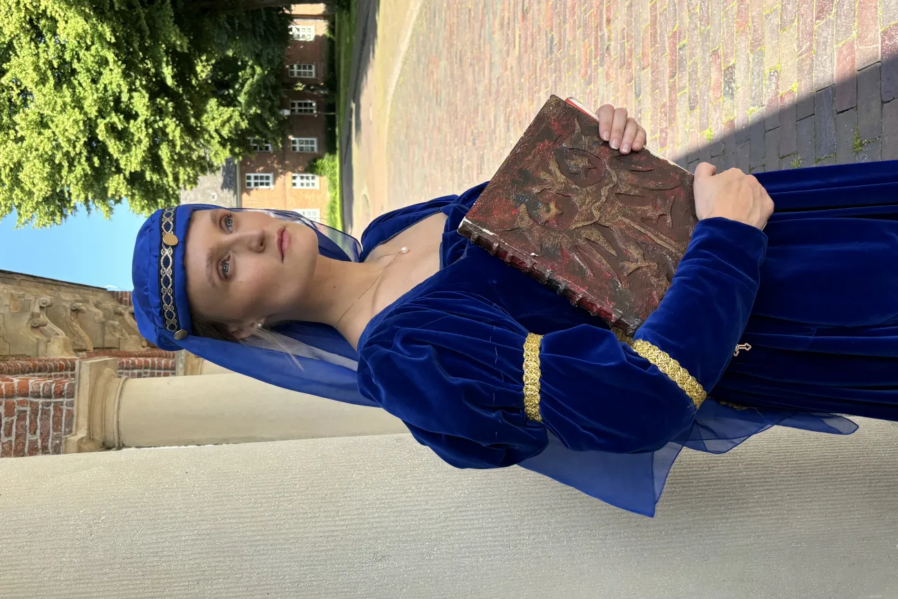 Frau in königsblauem Mittelalterkleid mit Buch steht vor historischem Gebäude in Greetsiel.