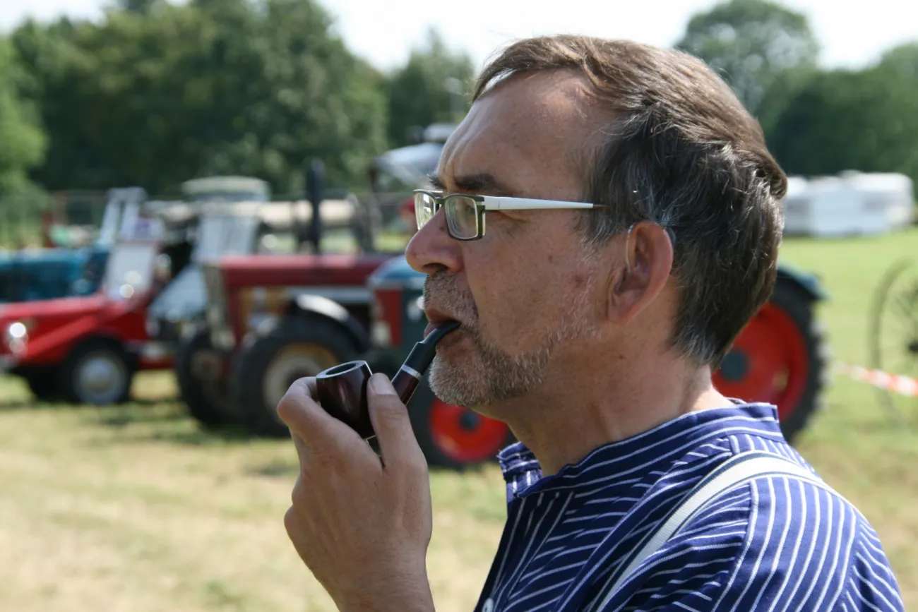 Georg Tjaden mit Pfeife im Profil vor historischen Traktoren auf einer Wiese.