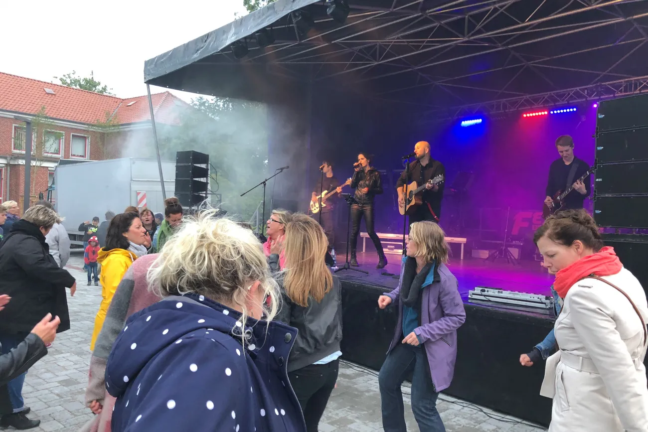 Eine Live-Band spielt auf einer Open-Air-Bühne, davor tanzen Menschen ausgelassen.