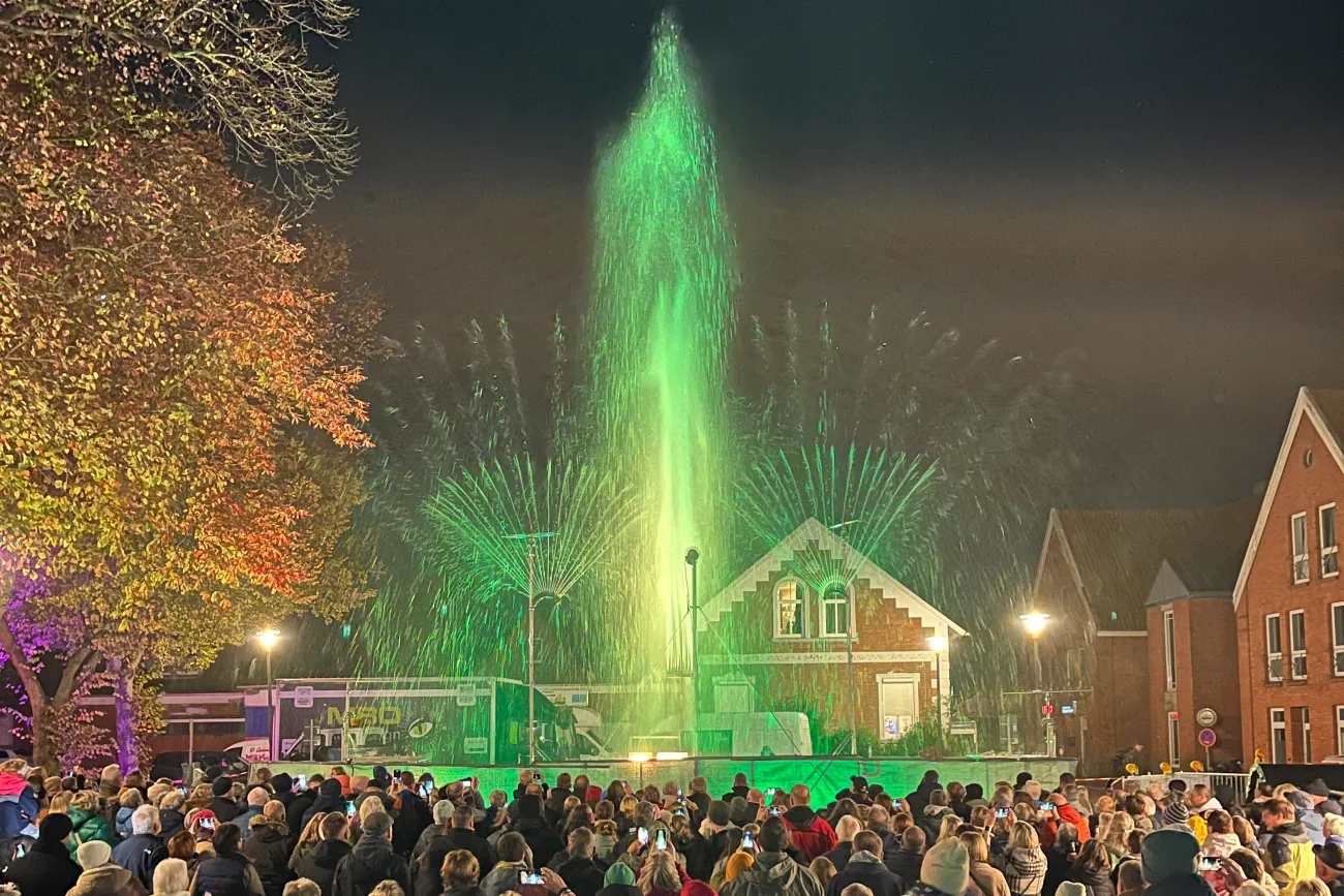 Menschenmenge beobachtet abends eine grün beleuchtete Wasser- und Lichtshow vor historischen Gebäuden