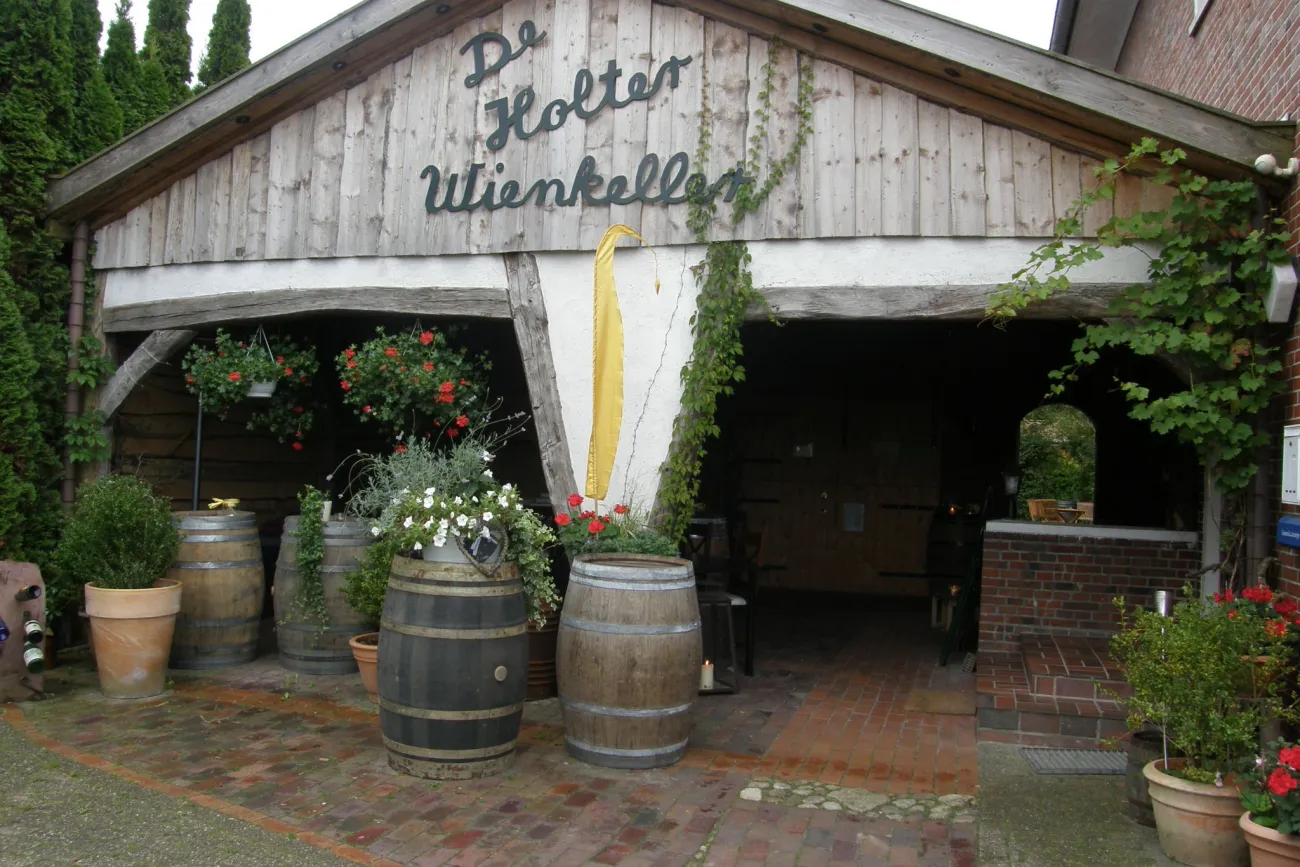 Eingang zum De Holter Wienkeller mit Holzfass-Dekoration und Pflanzen in Töpfen