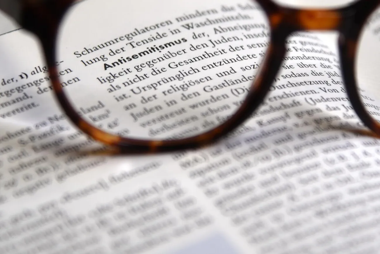 Brille fokussiert den Lexikonbegriff Antisemitismus auf einer aufgeschlagenen Seite.