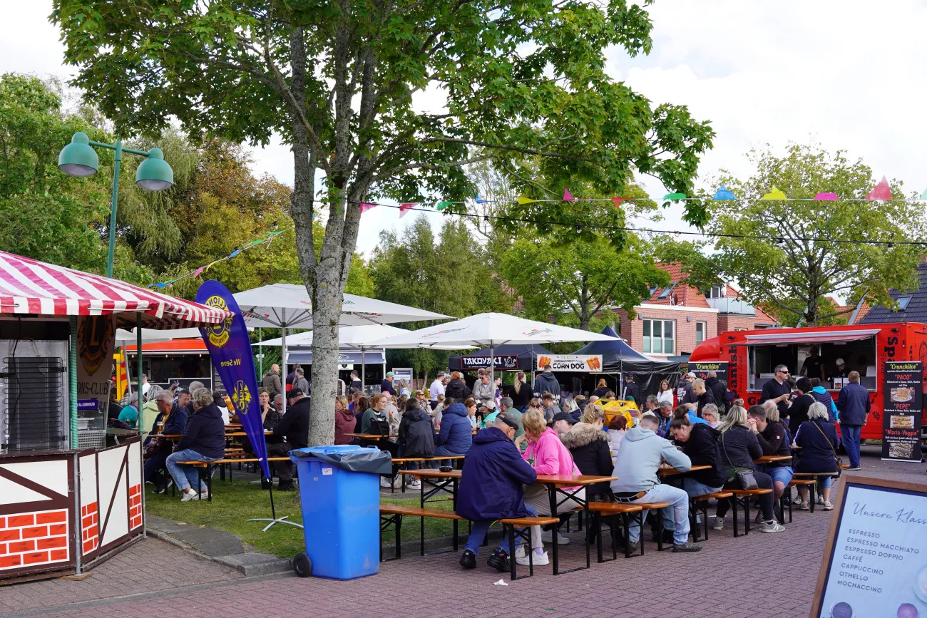 Menschen sitzen an Holzbänken zwischen Foodtrucks und bunten Fahnen beim Street Food Festival.