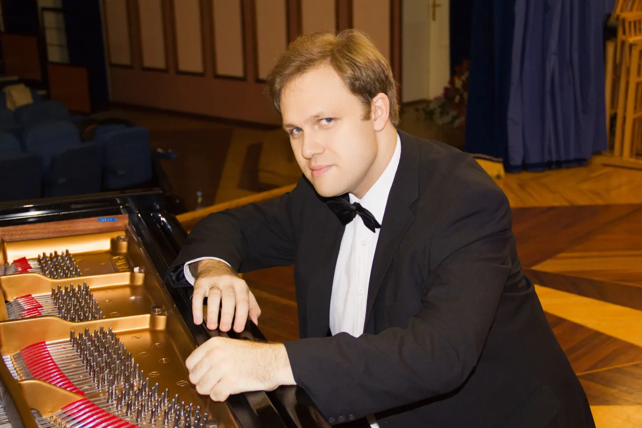 Pianist Alexey Chernov im schwarzen Anzug mit Fliege lehnt entspannt am Flügel.