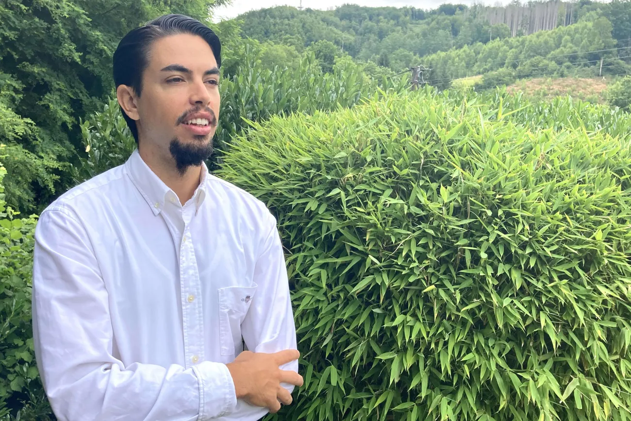 Pianist Rubén Russo im weißen Hemd vor einer grünen Hecke und Waldlandschaft.