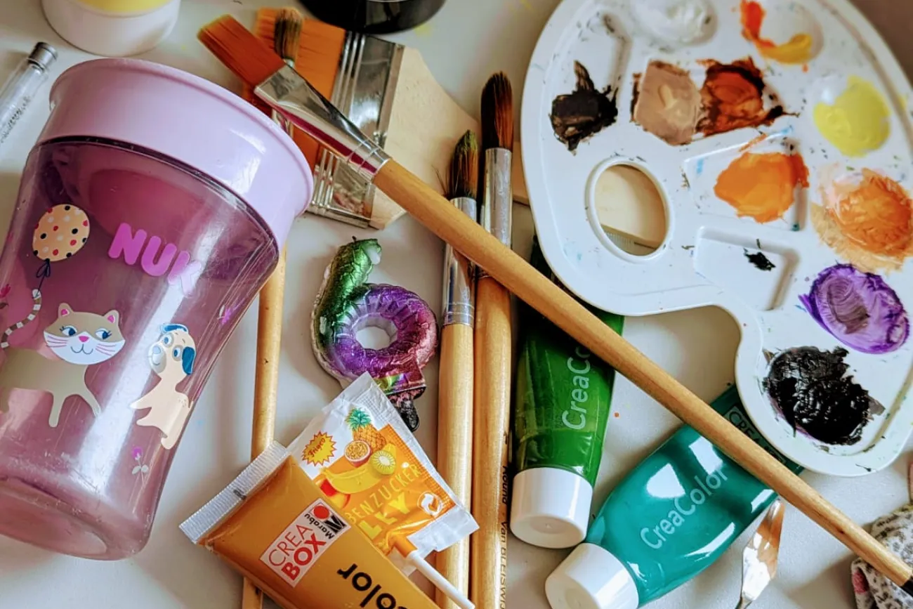 Pinsel, Acrylfarben, Mischpalette und ein Trinkbecher liegen bereit für die kreative Auszeit.