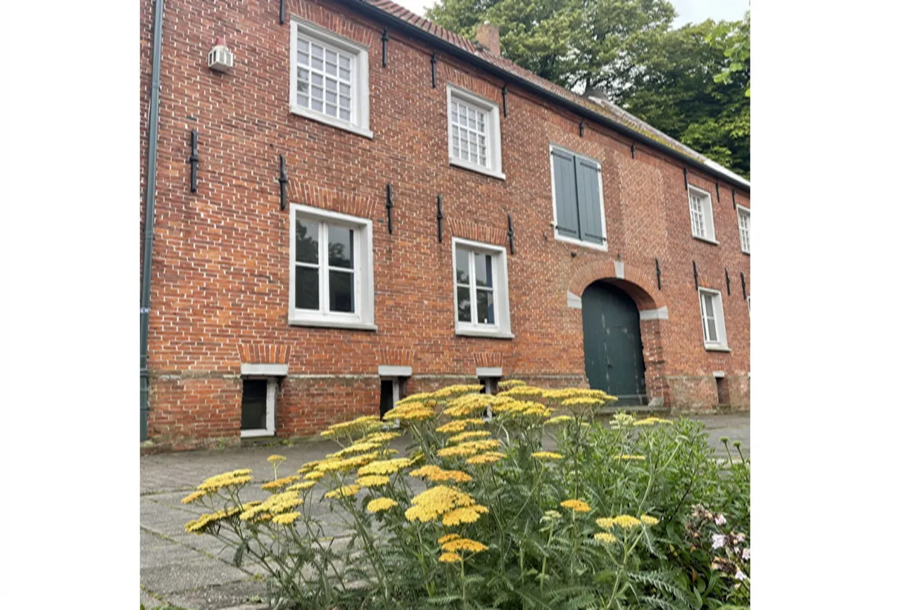 Historisches Backsteingebäude mit weißen Fenstern und gelben Blumen im Vordergrund.