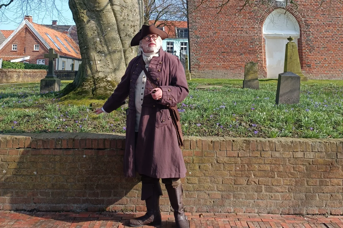 Hafenmeister Quirinus im historischen Gewand mit Dreispitz vor der alten Backsteinkirche.