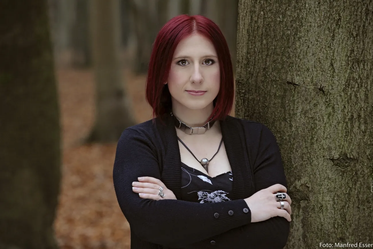 Auf dem Bild sieht man Lydia Benecke in einem Wald angelehnt an einem Baum.