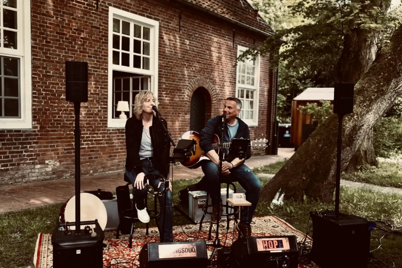 Sängerin und Gitarrist des Duos HoPe spielen live im Freien vor einem alten Backsteingebäude.