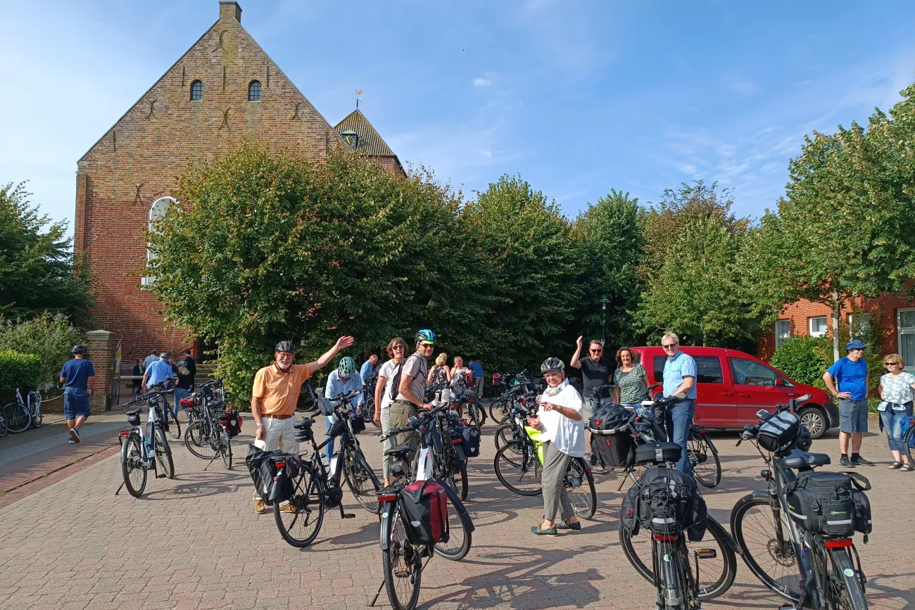 Eine Gruppe Radfahrer pausiert während der Krummhörner Kirchturm-Tour vor der Kirche in Uttum.