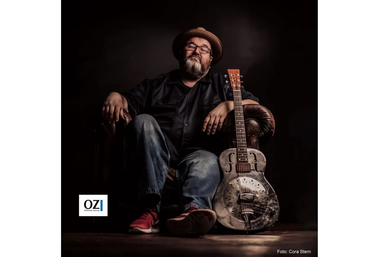 Bluesmusiker Michael van Merwyk sitzt mit Hut und Resonatorgitarre im dunklen Studio.
