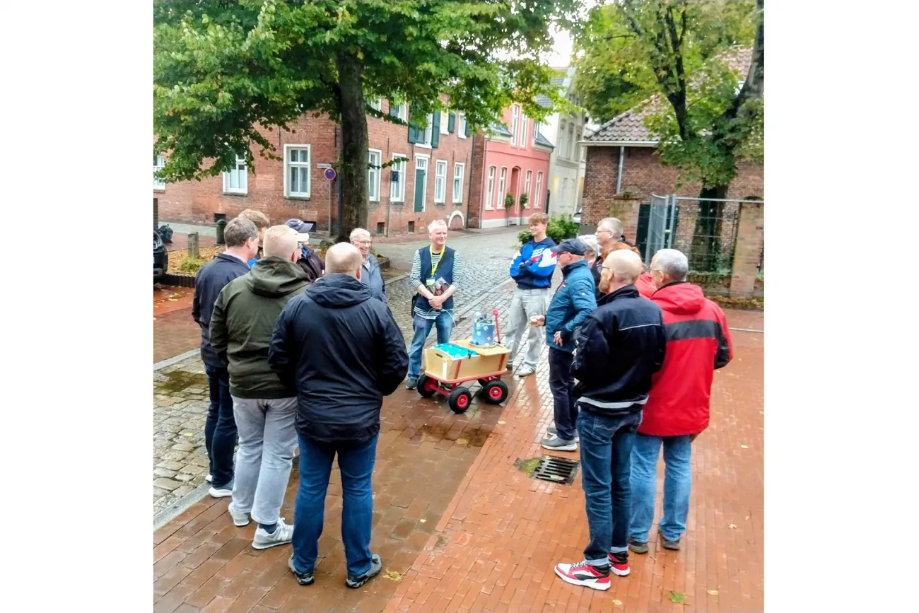 Gruppe bei einer Bierführung in der Leeraner Altstadt mit Bollerwagen auf nassem Pflaster.