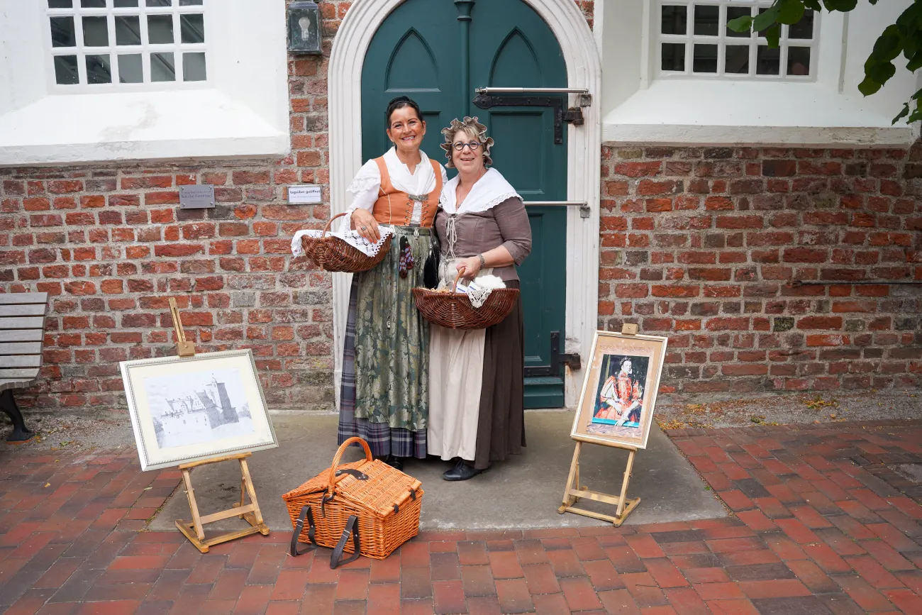 Daje und Geeske in historischen Kostümen vor Backsteinhaus in Greetsiel.