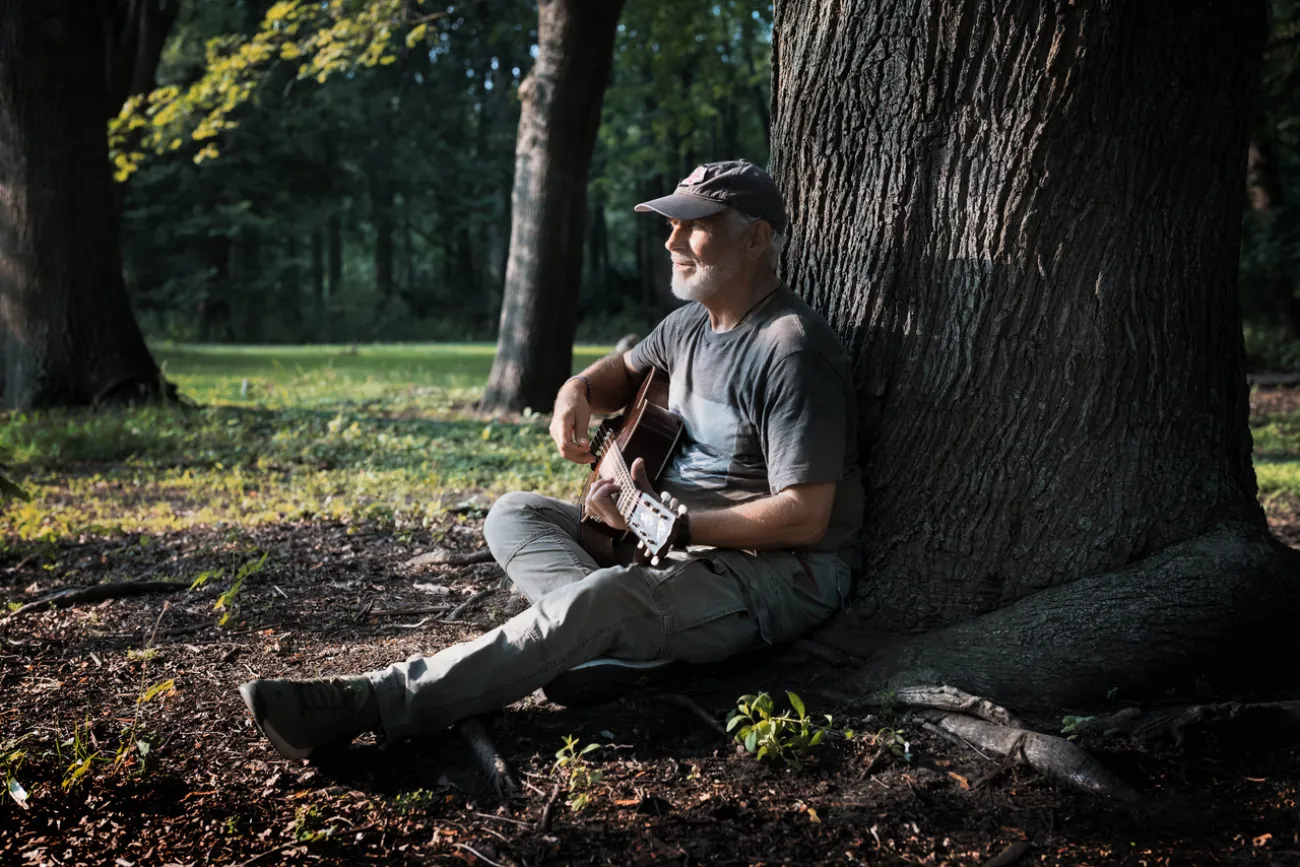 Gitarrist sitzt im Wald an einem Baumstamm und spielt im Sonnenlicht.