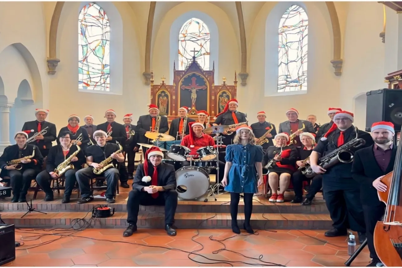 Bigband mit Weihnachtsmützen, Sängerin und Instrumenten vor dem Kirchenaltar.