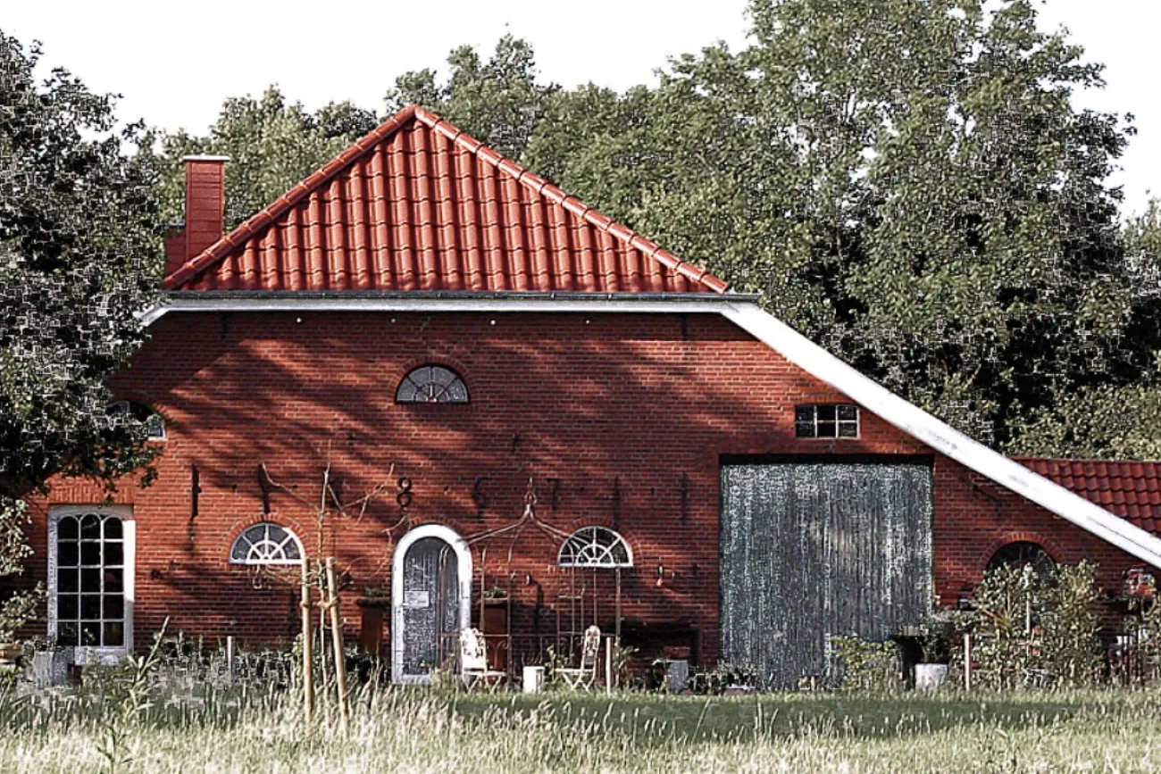 Rotes Backsteinhaus mit rotem Ziegeldach, Wiese und Bäumen am Atelier Glockenhaus