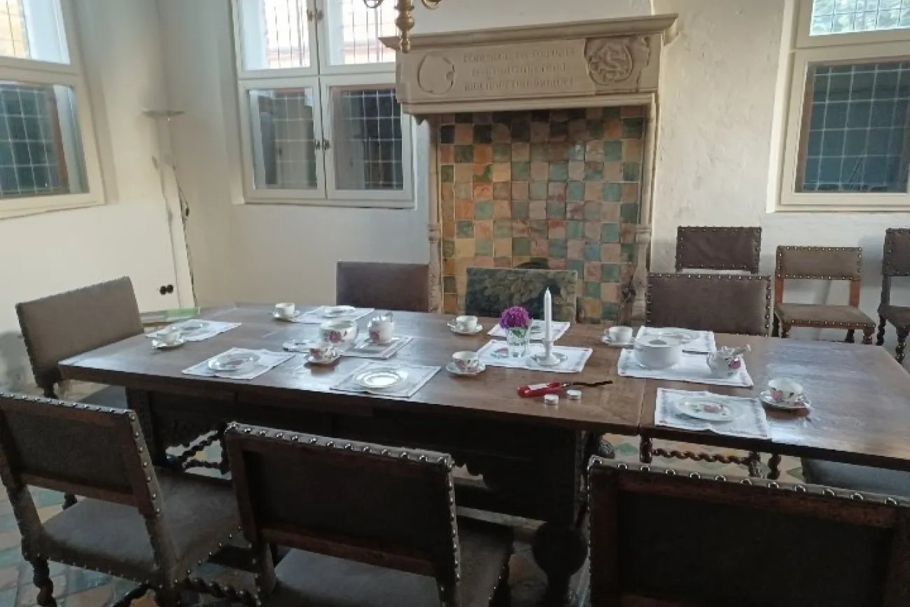 Holztisch mit Teeservice und Blumen vor historischem Kamin im Steinhaus Greetsiel.