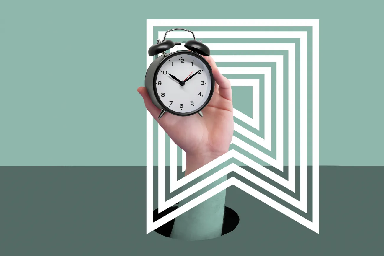 Eine Hand taucht aus einem Loch im Tisch auf und hält einen Wecker.