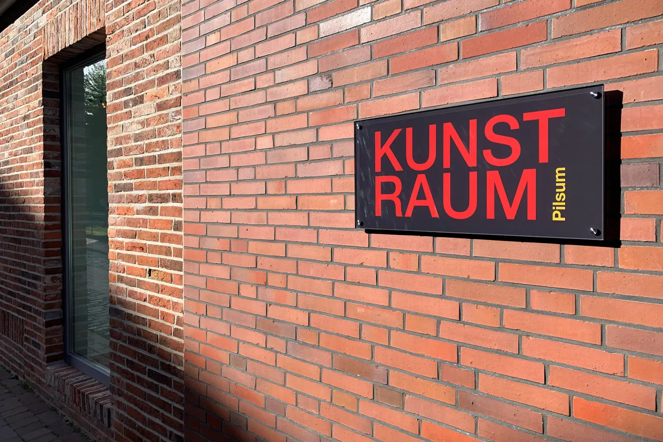 Das Foto zeigt das Schild Kunstraum Pilsum an der dortigen Hauswand.
