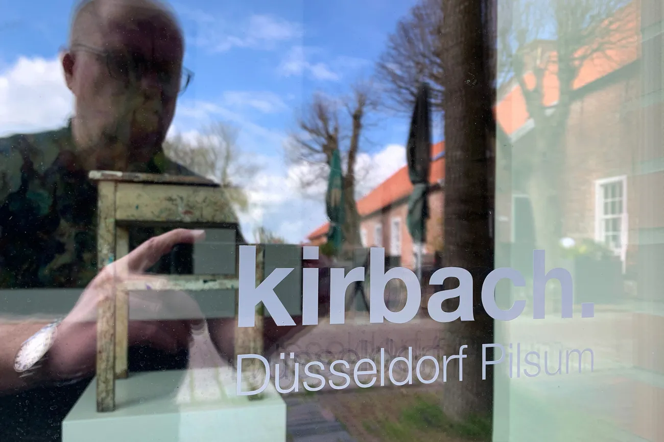 Das Foto zeigt den Galeristen und Kunsthändler André Kirbach, wie er die Beschriftung der Schaufensterscheibe fotografiert. Dort steht Kirbach Düsseldorf Pilsum.