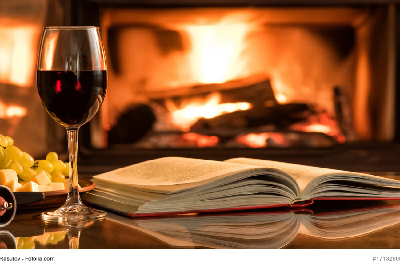 Offenes Buch mit einem Glas Wein, Feuer im Kamin im Hintergrund