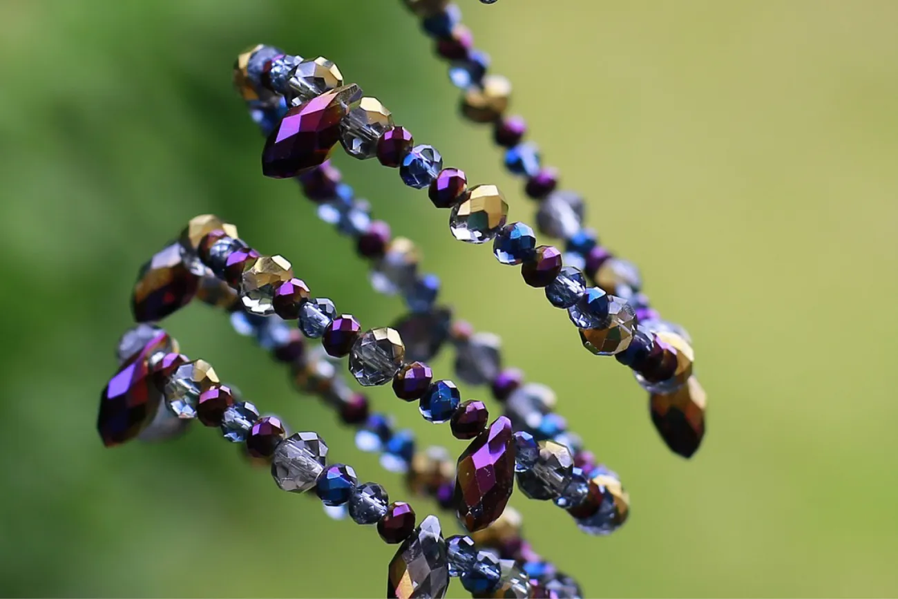 spiralförmiger Schmuckarmreif mit violetten und blauen Perlen auf grünen Hintergrund