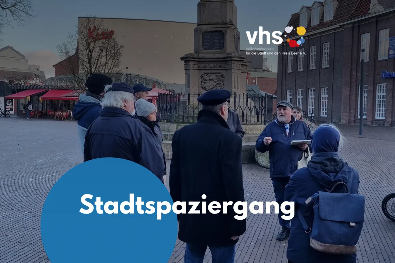 Eine Gruppe von Teilnehmenden hört während eines geführten Stadtspaziergangs in Leer einem Stadtführer vor einem Denkmal aufmerksam zu. 