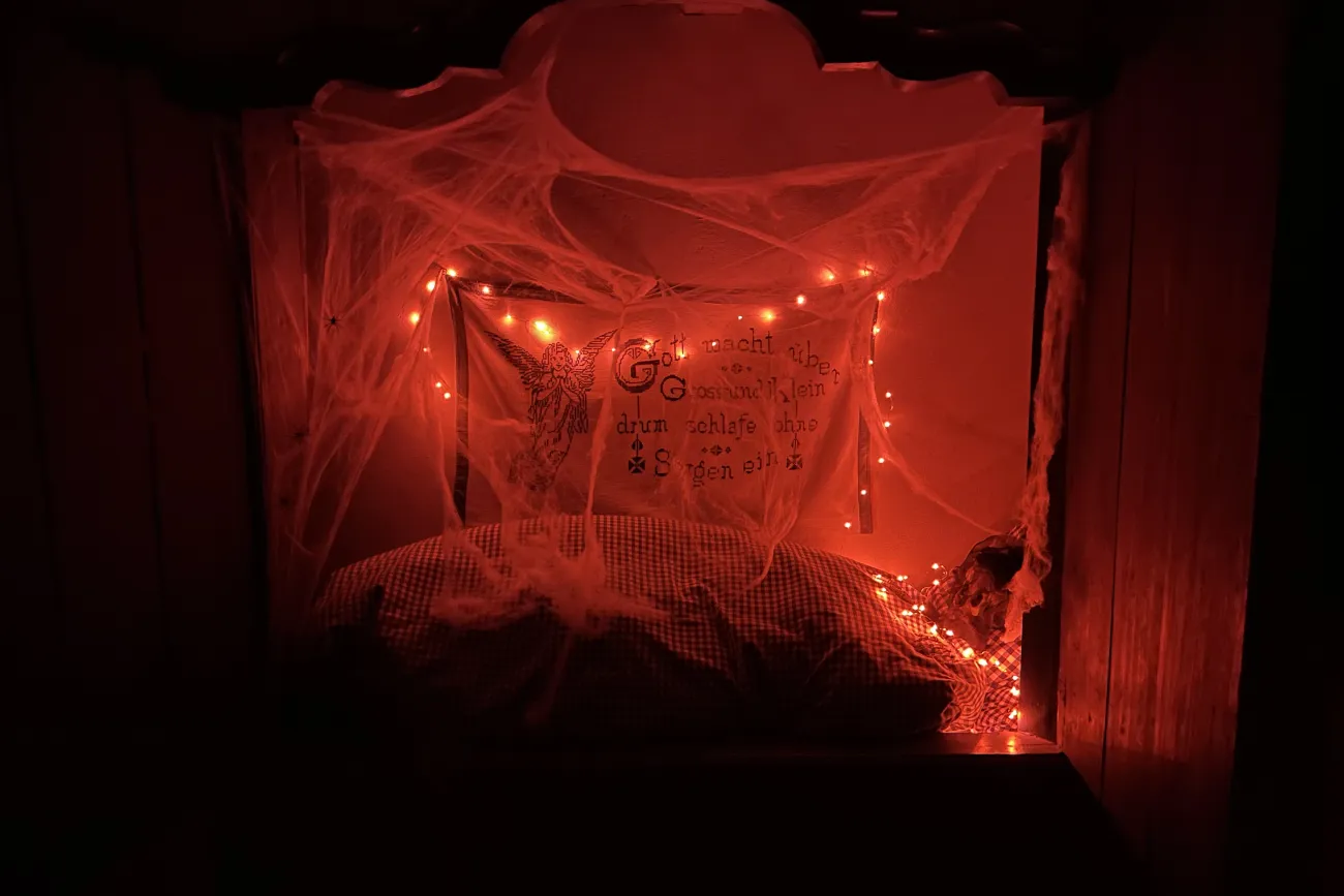 Rotes Licht, kleine Butze mit Bettzeug, Spinnenweben, eigenartiger Gestalt im Bett
