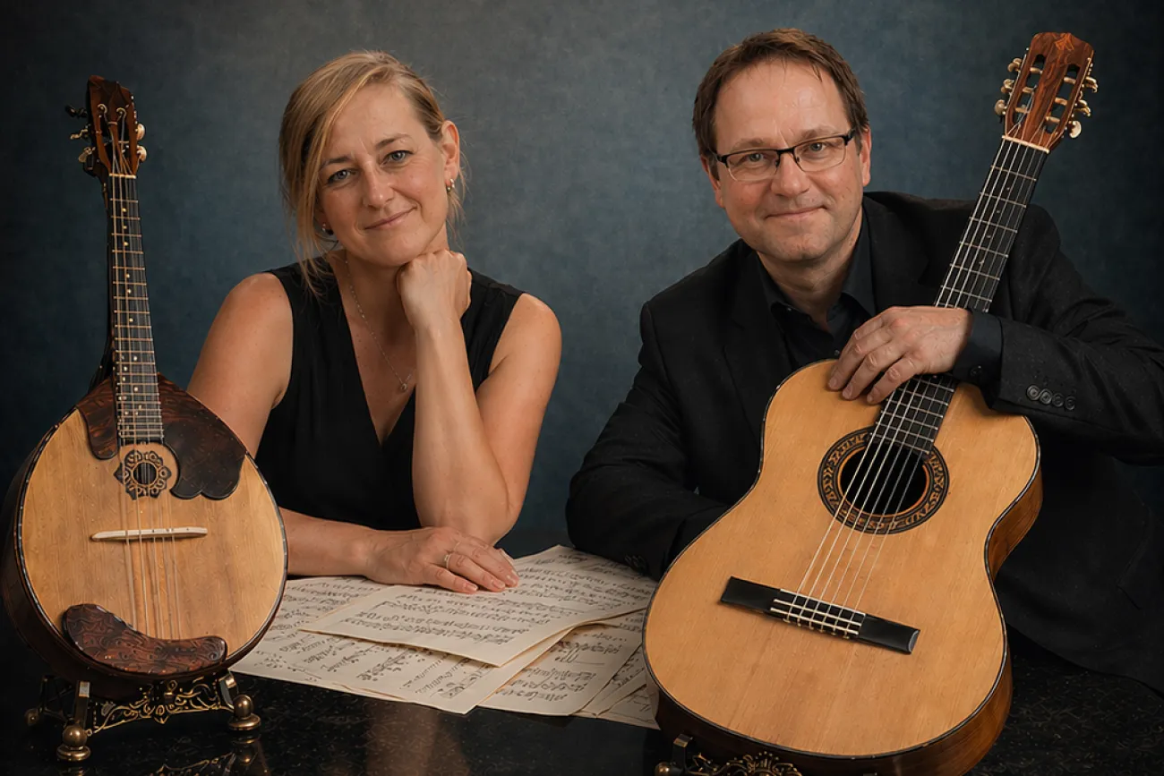 Eine Musikerin mit Domra und ein Musiker mit Gitarre sitzen am Tisch und blicken freundlich