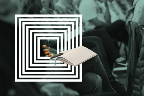 Nahaufnahme eines Publikums – eine Teilnehmerin hält ein Buch, Handy und einen Stift in ihrem Schoß