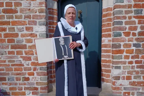 Frau in historischer Tracht hält ein Porträt von Gräfin Anna von Ostfriesland vor Backsteinmauer.