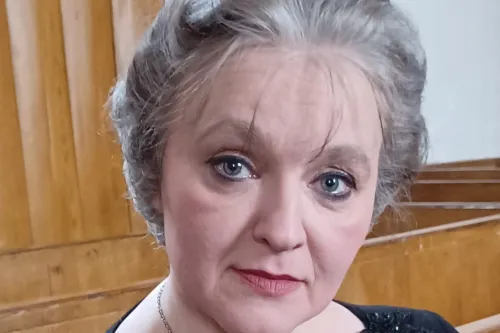 Frau in historischer Kleidung mit grauer Hochsteckfrisur in einem Holzsaal, Porträtaufnahme.