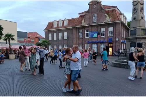 Viele Menschen tanzen paarweise auf dem Denkmalplatz neben einem großen Denkmal.