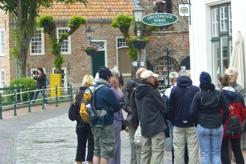 Eine Gruppe Erwachsener steht bei einer Dorfführung auf einer gepflasterten Gasse in Greetsiel.
