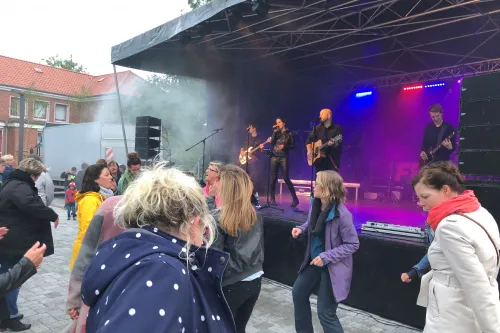 Eine Live-Band spielt auf einer Open-Air-Bühne, davor tanzen Menschen ausgelassen.