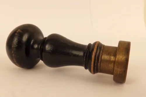 Stempel mit schwarzem Holzgriff und Messingplatte liegt auf hellem Untergrund
