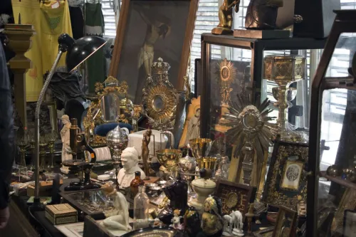 Antikmarktstand mit religiösen Objekten, Leuchtern, Figuren, Büchern und Glasvitrinen.