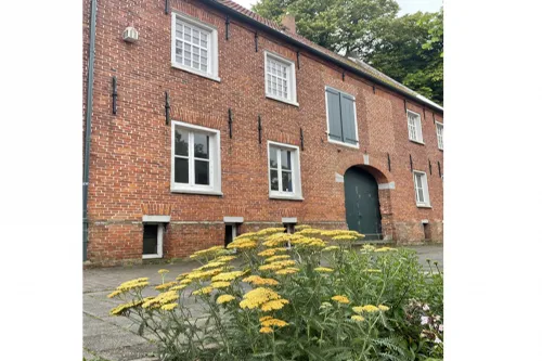 Historisches Backsteingebäude mit weißen Fenstern und gelben Blumen im Vordergrund.