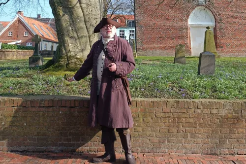 Hafenmeister Quirinus im historischen Gewand mit Dreispitz vor der alten Backsteinkirche.