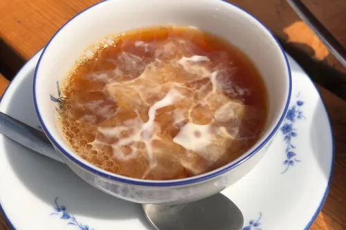 Ostfriesentee mit einem Sahnewölkchen in einer weiß-blauen Tasse auf einem Holztisch.