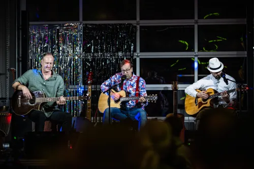 Drei Musiker spielen Gitarre und Bass auf einer Bühne vor Publikum.
