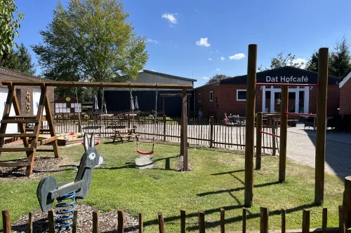 Spielplatz vor Dat Hofcafé mit Schaukel, Wipptier und Sitzplätzen bei Sonne.