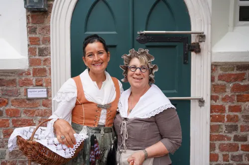 Daje und Geeske in Tracht mit Korb vor grüner Tür in Greetsiel.
