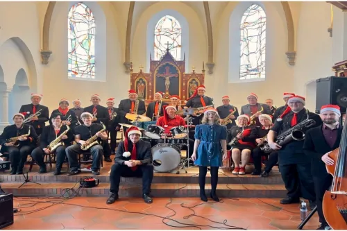 Bigband mit Weihnachtsmützen, Sängerin und Instrumenten vor dem Kirchenaltar.