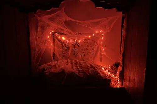 Rotes Licht, kleine Butze mit Bettzeug, Spinnenweben, eigenartiger Gestalt im Bett